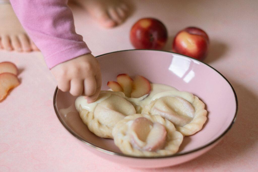 Pierogi mit Pflaumen: Herbstliches Rezept; Kleinkind greift nach gekochten Pflaumen-Piroggen