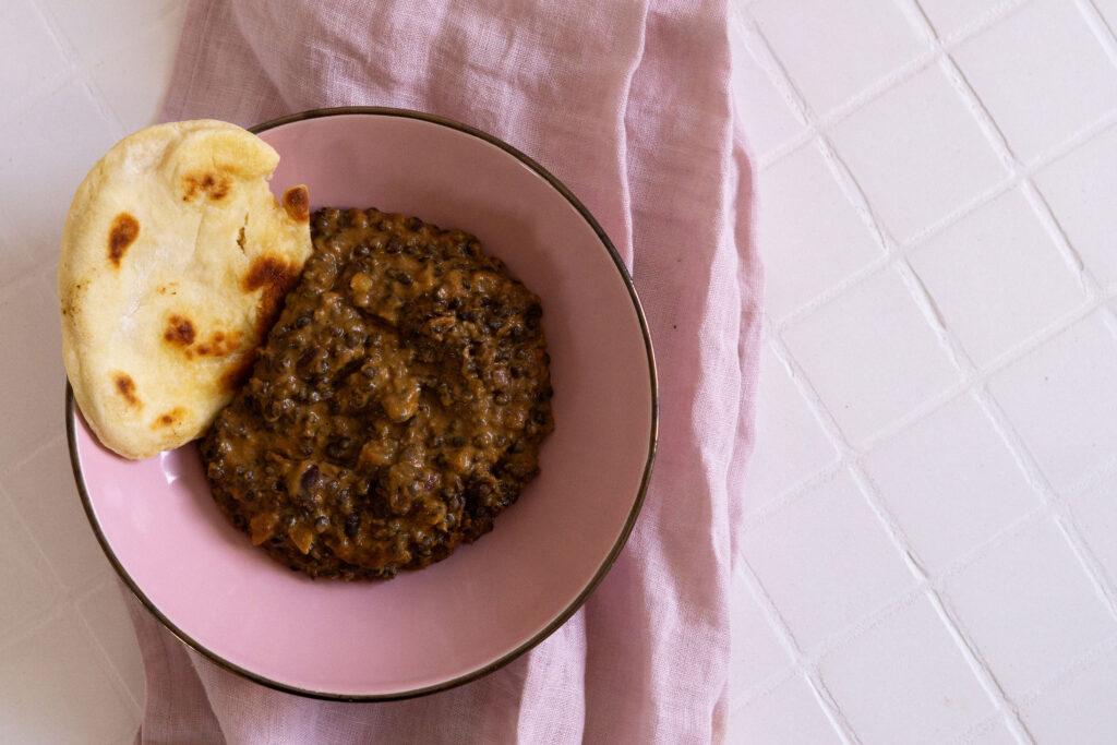 Indisches Linsengericht Dal Makhani auf einem rosa Teller von oben fotografiert mit Pfannenbrot im Hintergrund